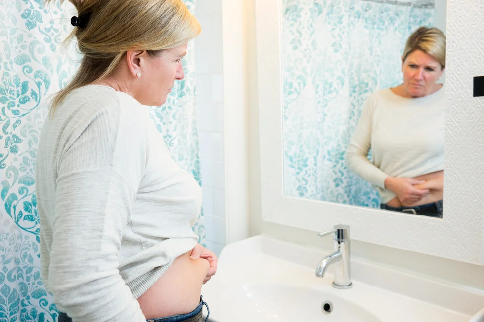 woman looking at her stomach in the mirror