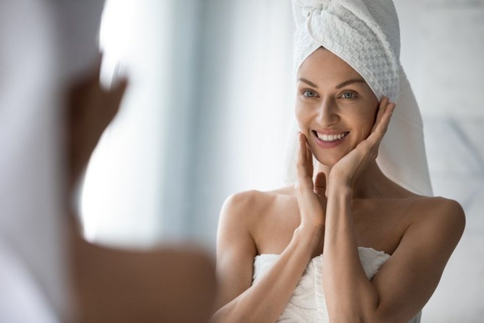 woman looks in mirror touches moisturized soft healthy face skin feels satisfied