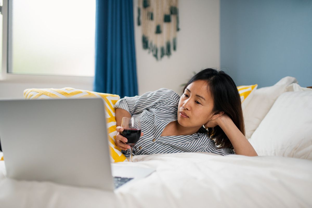 Woman lying on her bed drinking wine watching TV