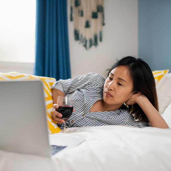 Woman lying on her bed drinking wine watching TV