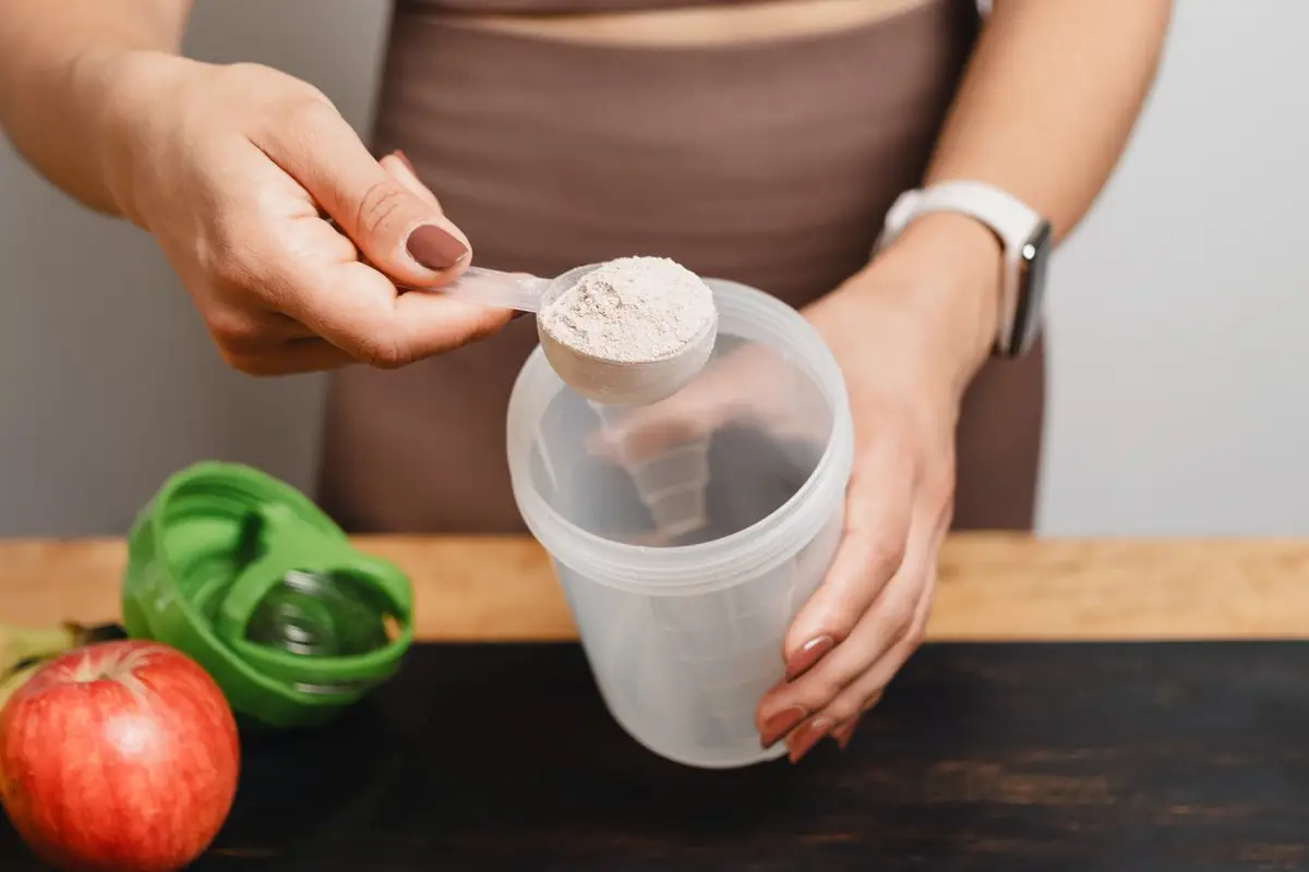 woman scooping creatine powder into a shaker