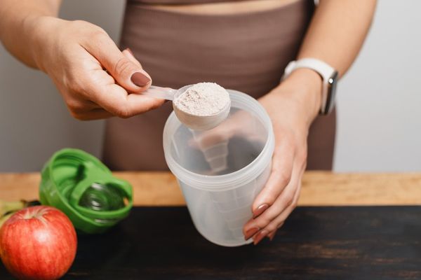 woman scooping creatine powder into a shaker
