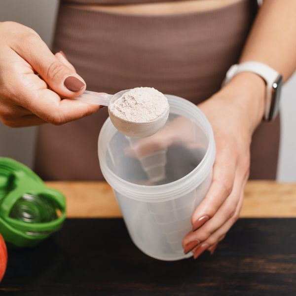 woman scooping creatine powder into a shaker