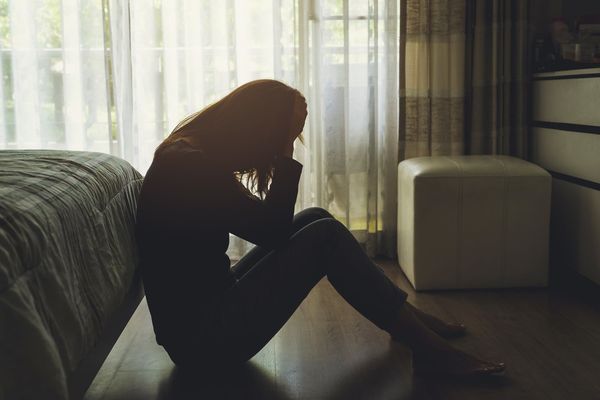 Woman sitting down on the ground upset holding her head in her hands
