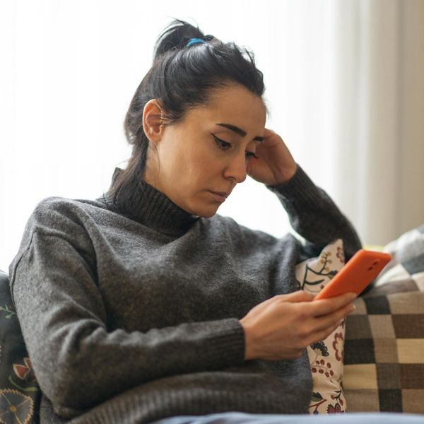 Woman sitting on a sofa and looking at mobile phone screen at home.