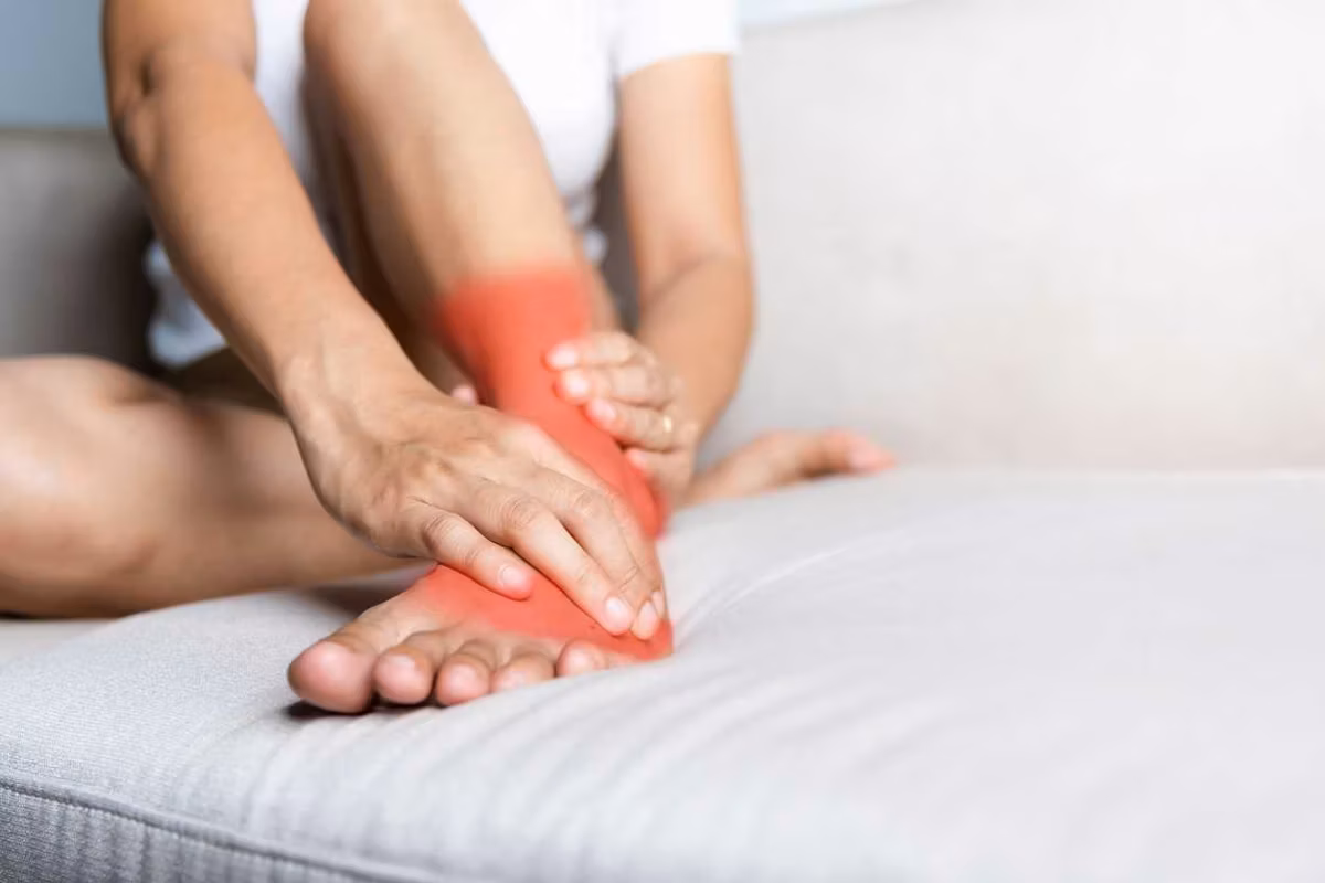 woman sitting on sofa hold her ankle injury feeling pain in her foot at home