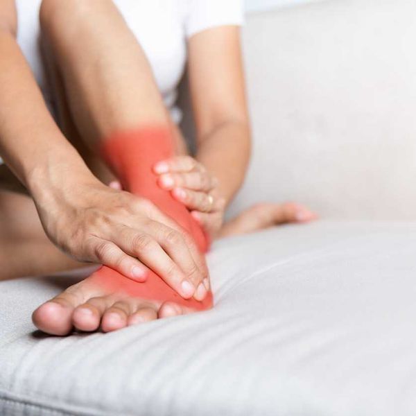 woman sitting on sofa hold her ankle injury feeling pain in her foot at home