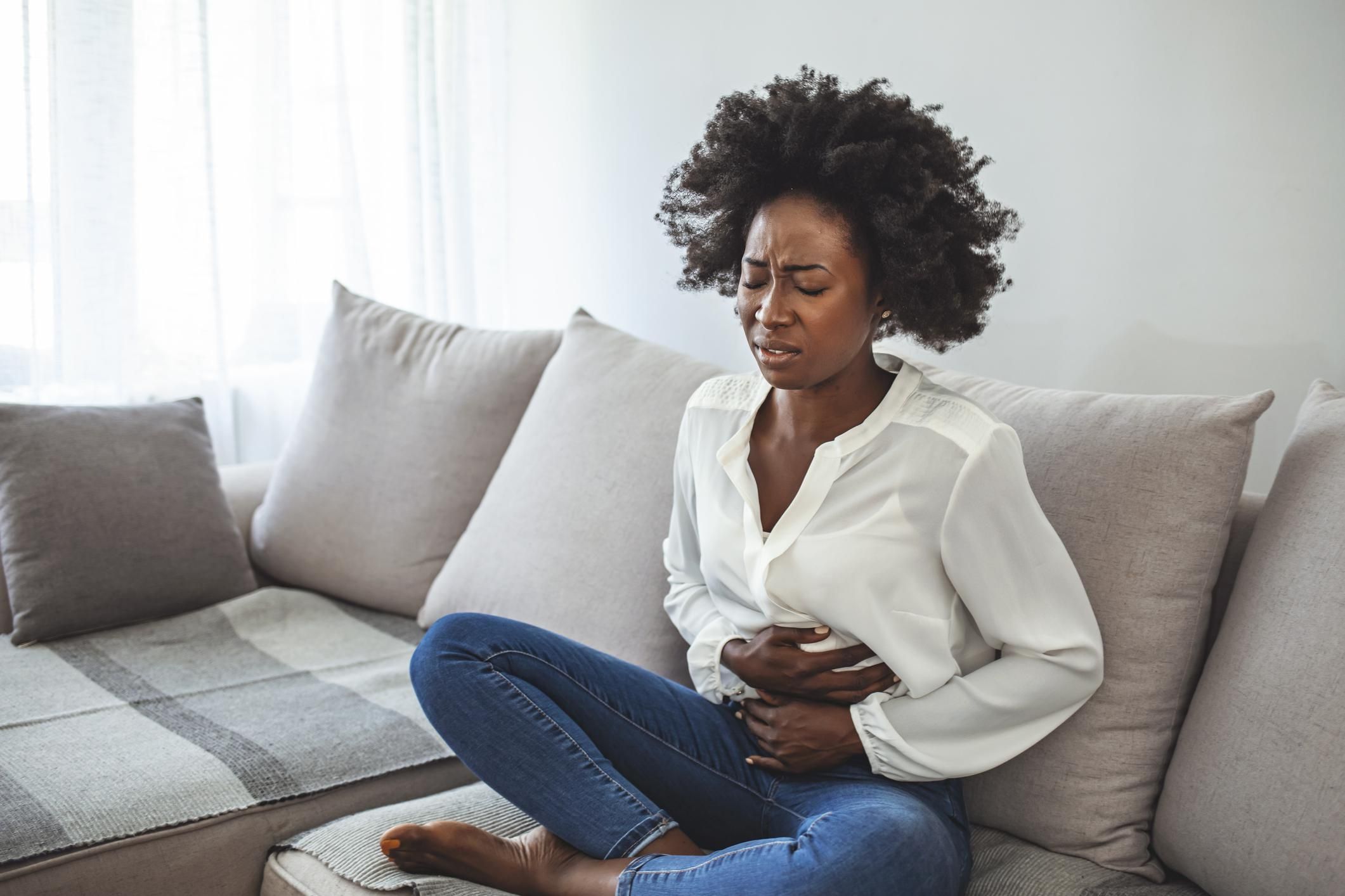 Woman Sitting On Sofa Suffering From Stomach Pain