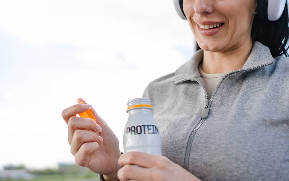 Woman smiling opening protein drink after outdoor workout