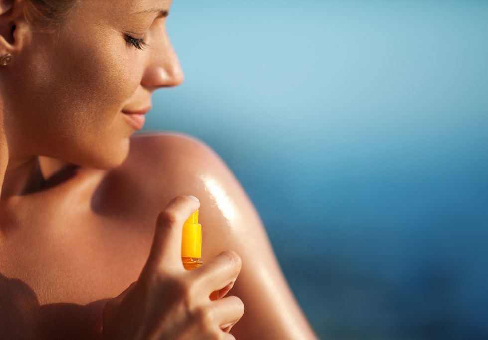woman spraying suntan lotion onto her shoulder