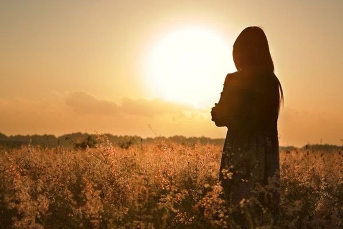 woman standing in a field looking at a sunset