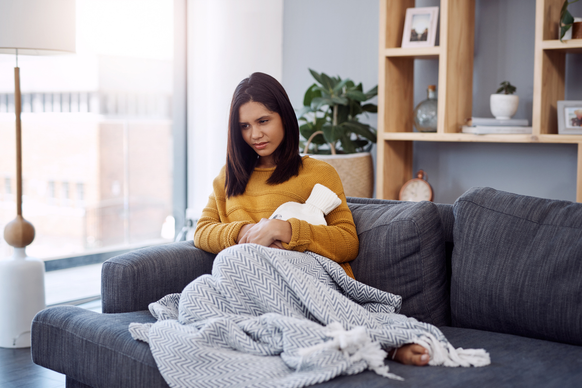 woman suffering from stomach cramps while sitting on a sofa at home
