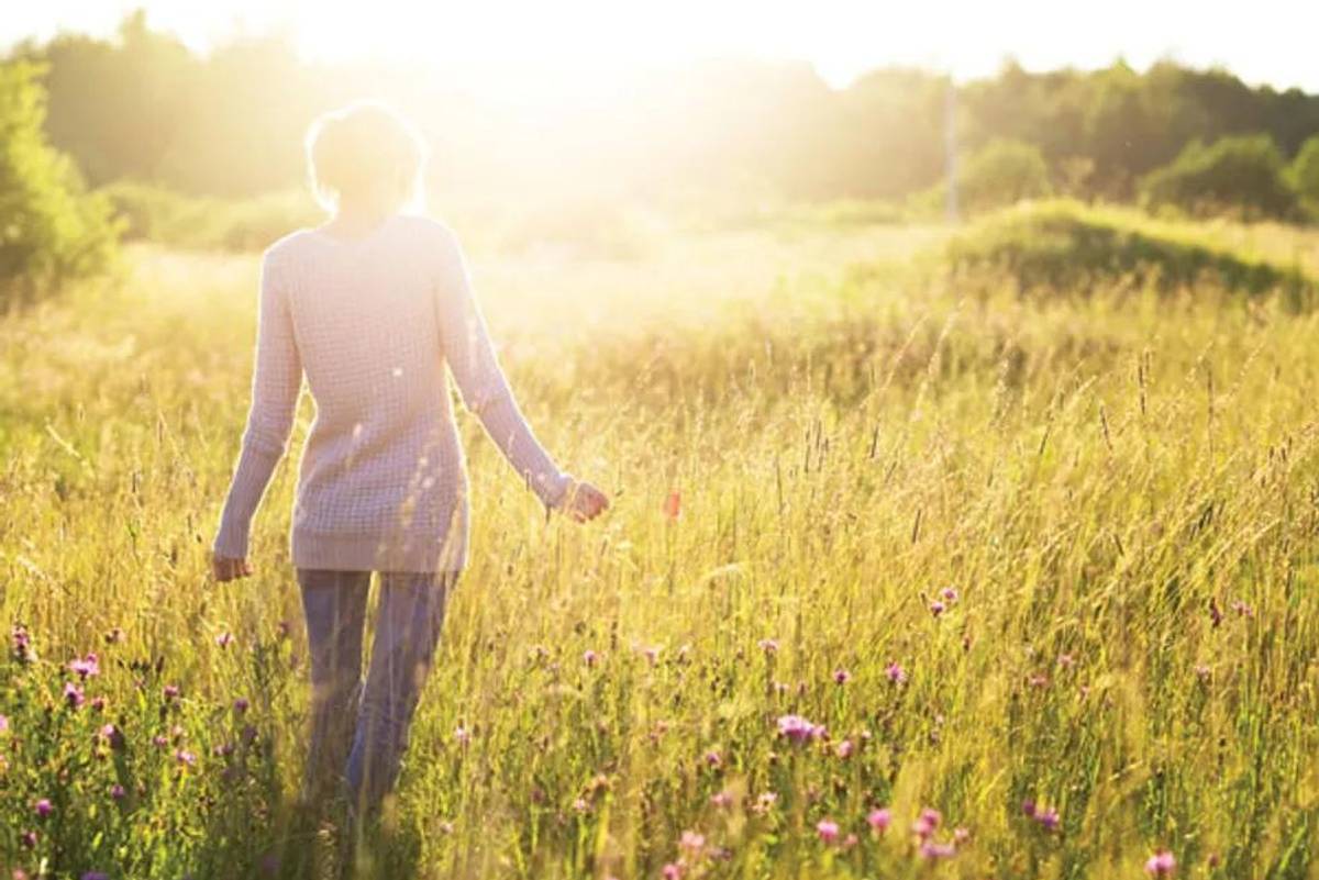 woman walking in the field toward the sun