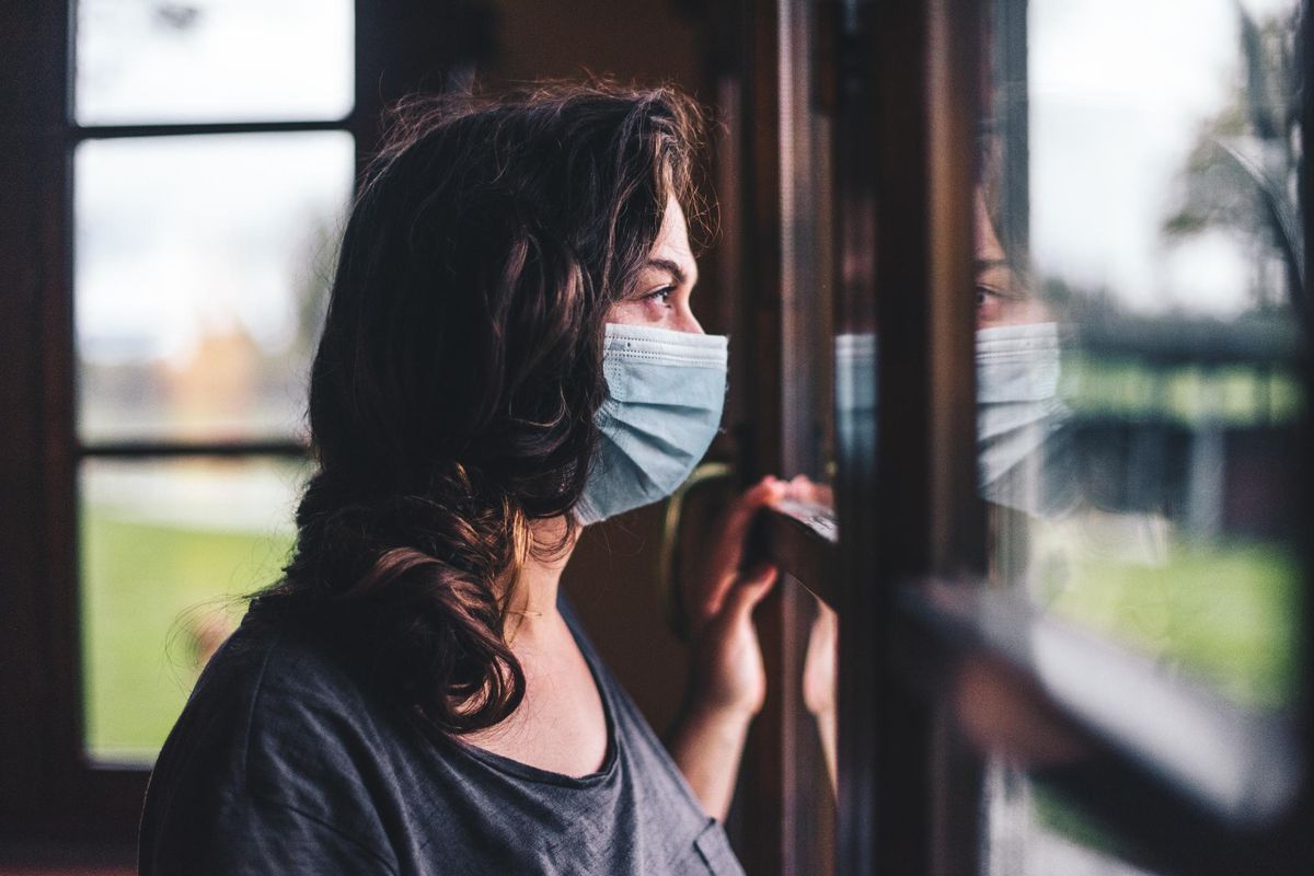 Woman wearing a blue surgical mask looking out the window