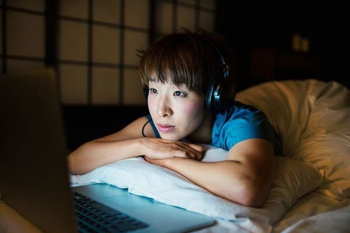 woman wearing headphones lying in bed watching tv on her laptop