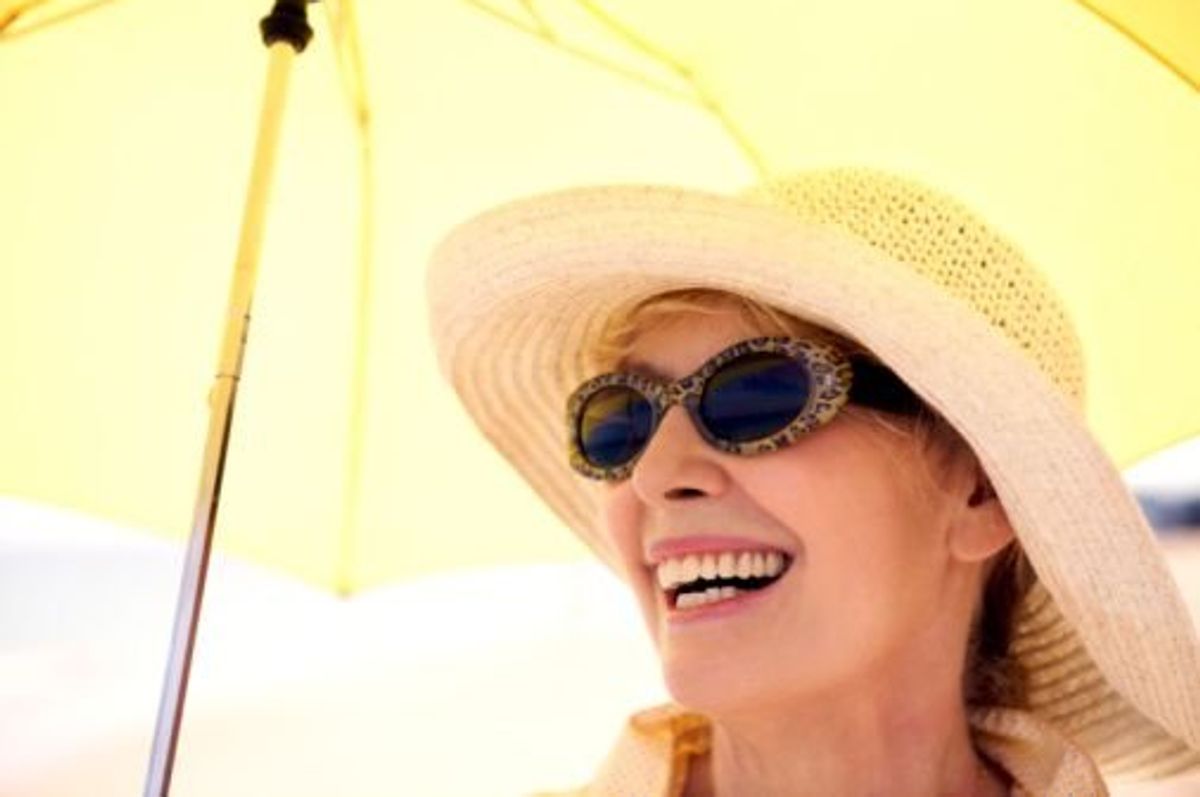 woman wearing sunglasses and sun hat sitting under an umbrella trying to protect her eyes from sun damage