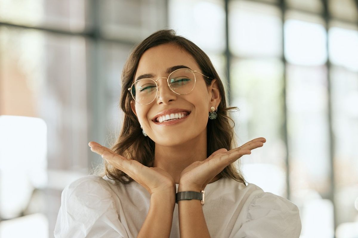 woman with glasses posing with her hands under her face showing her smile in an office