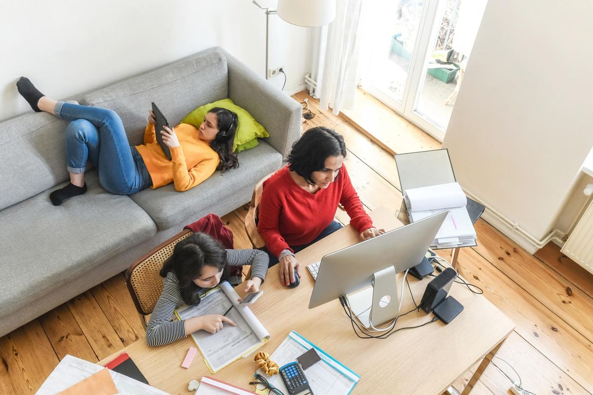 woman working at home in living room, daughters doing home work and hanging around