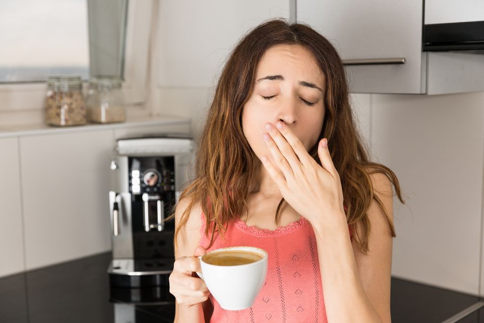 Woman yawning and drinking coffee in the kitchen in the morning