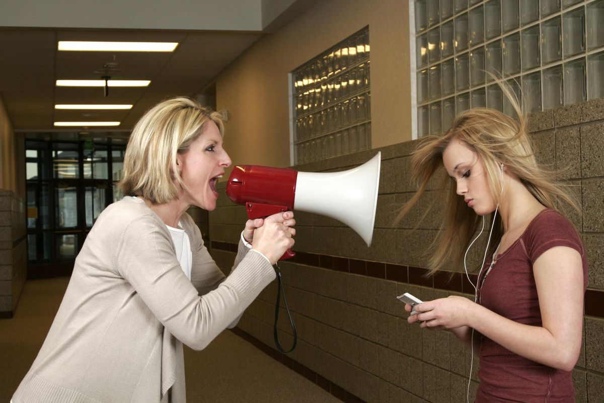 Woman yelling through a bullhorn at an unfazed teenage girl