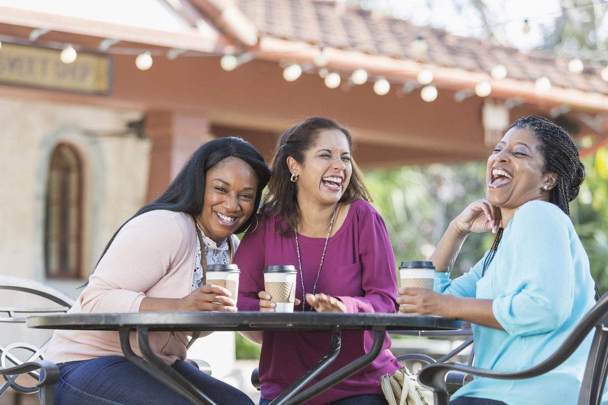Women at sidewalk cafe drinking coffee, laughing
