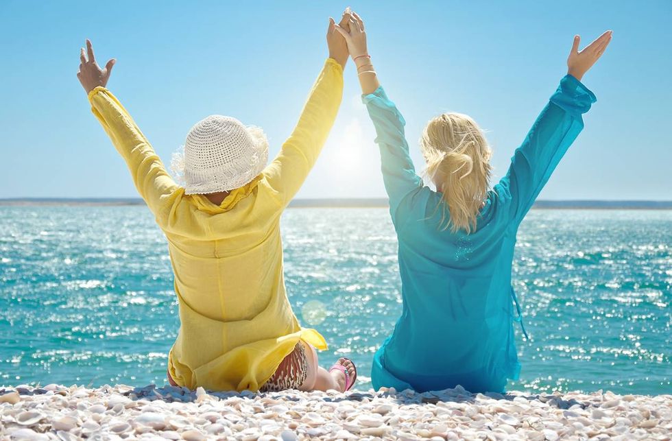 women wearing upf shirts with arms raised sitting on beach