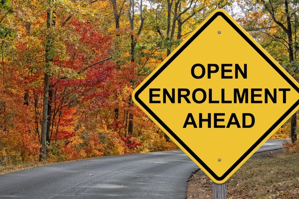Yellow road sign on a tree-lined street reads: open enrollment ahead.