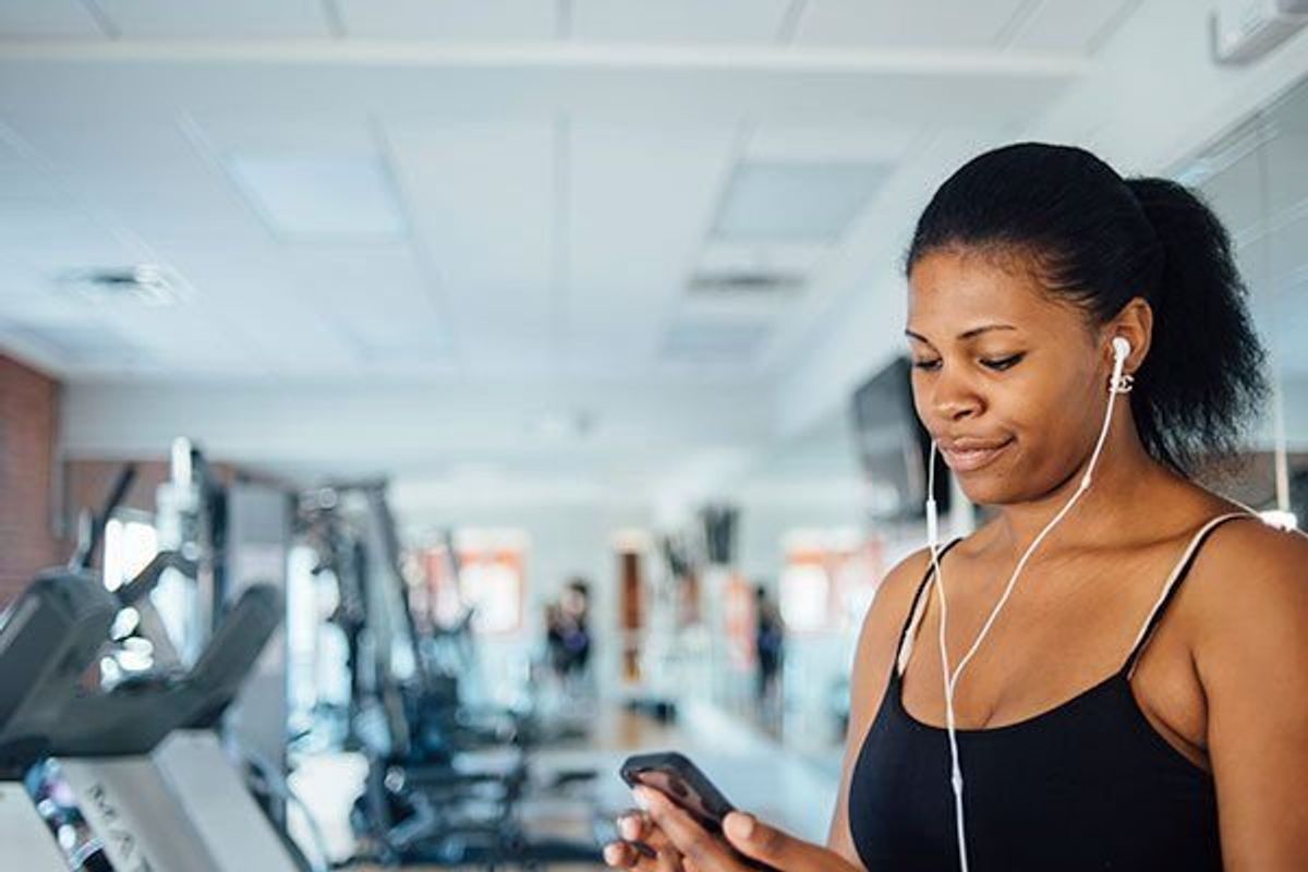 Young black women checking her fitness app stats at the gym while listening to music.