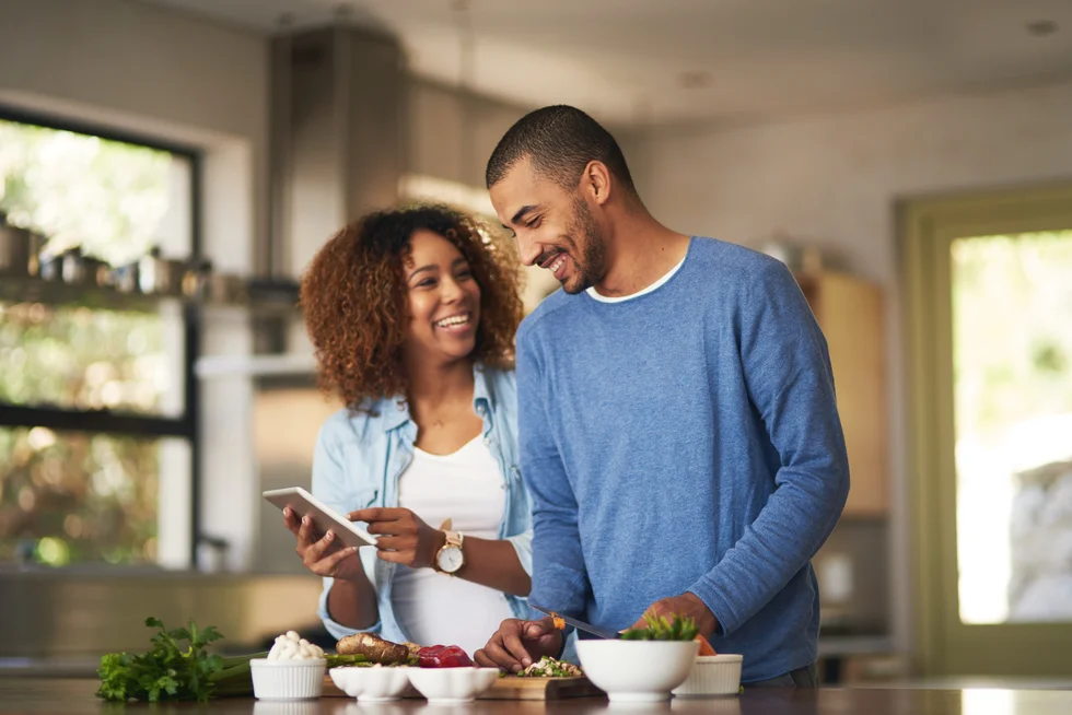 young couple using a digital tablet while preparing a healthy meal together at home