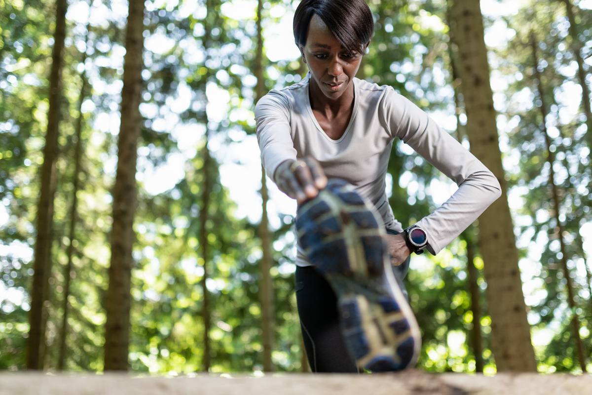Young female runner warming up before running in forest