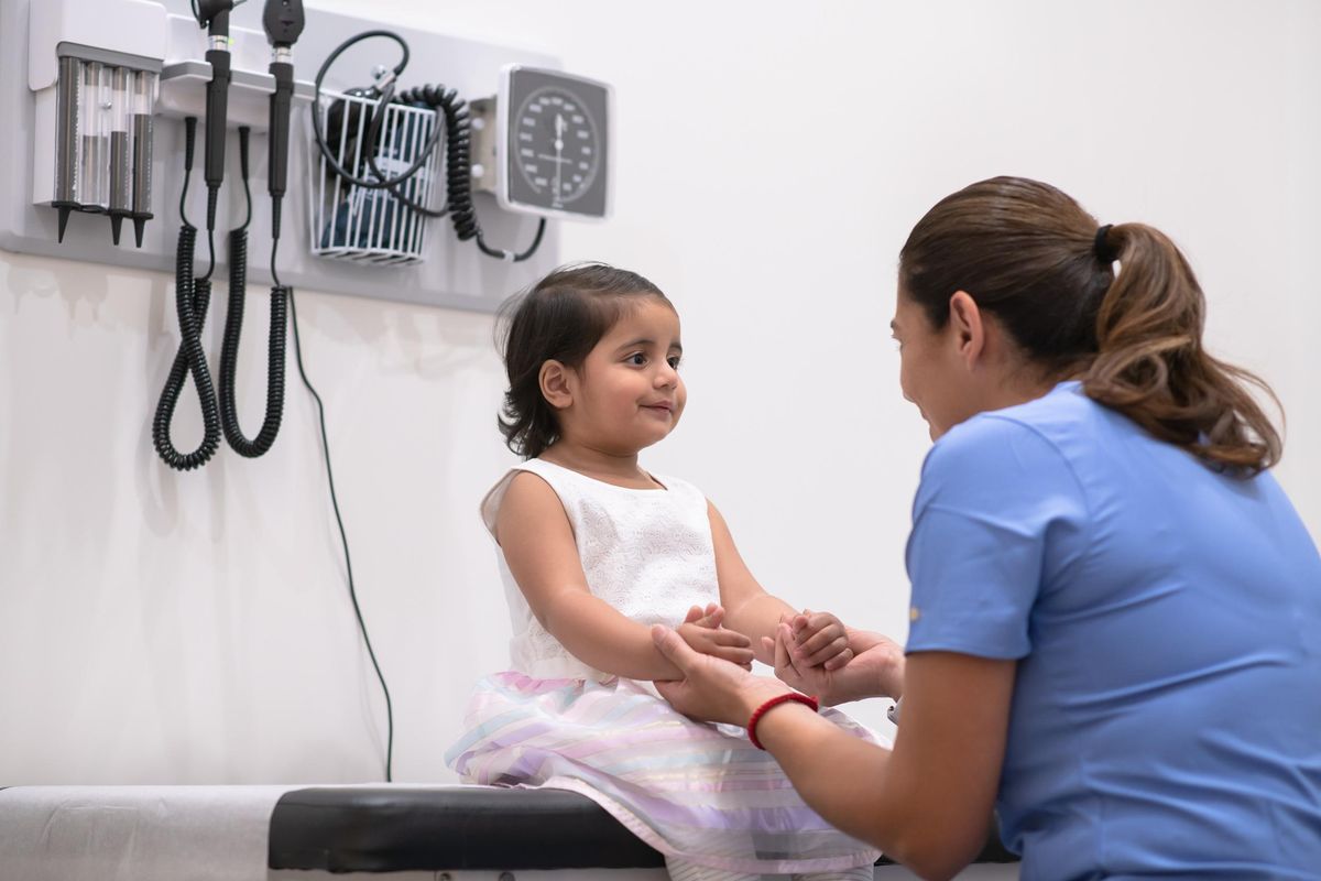 young girl with von Willebrand Disease looks at her doctor with a smile while sitting on the examination table.