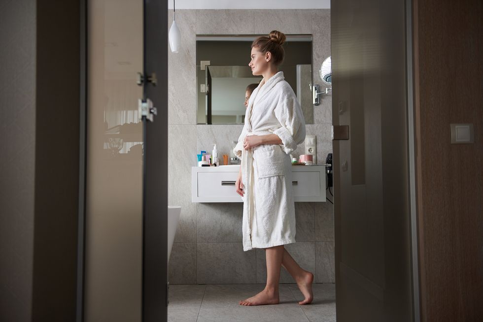young smiling woman in white bathrobe staying in bathroom near wash basin
