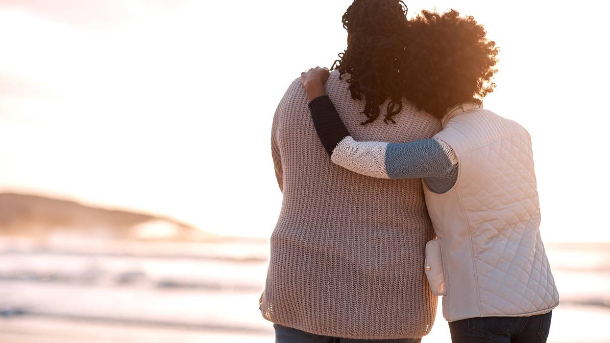 young woman embracing her mother while watching the sunset at the beach