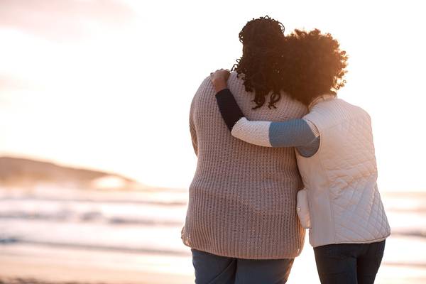 young woman embracing her mother while watching the sunset at the beach