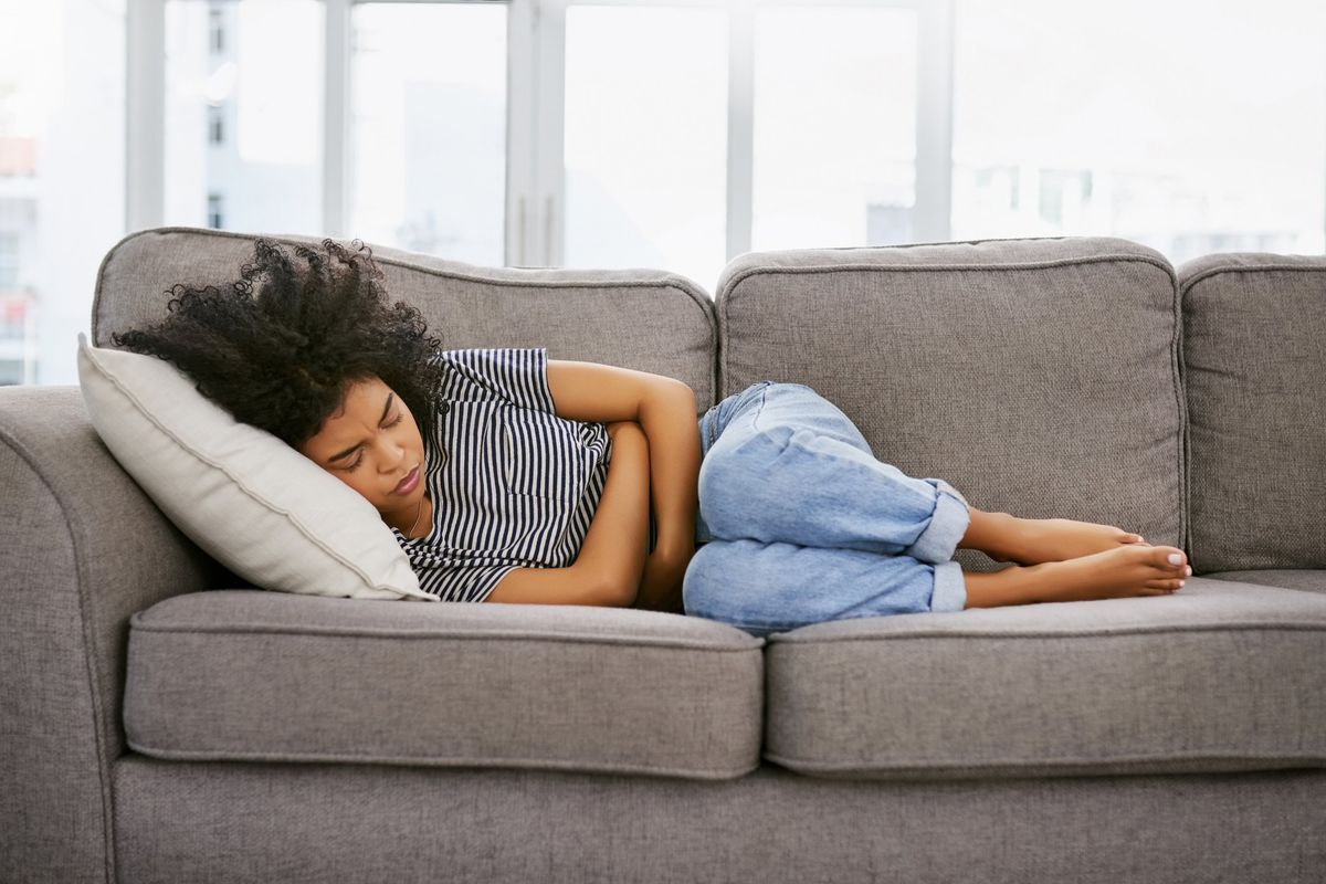 young woman experiencing pelvic pain from fibroids on the sofa at home