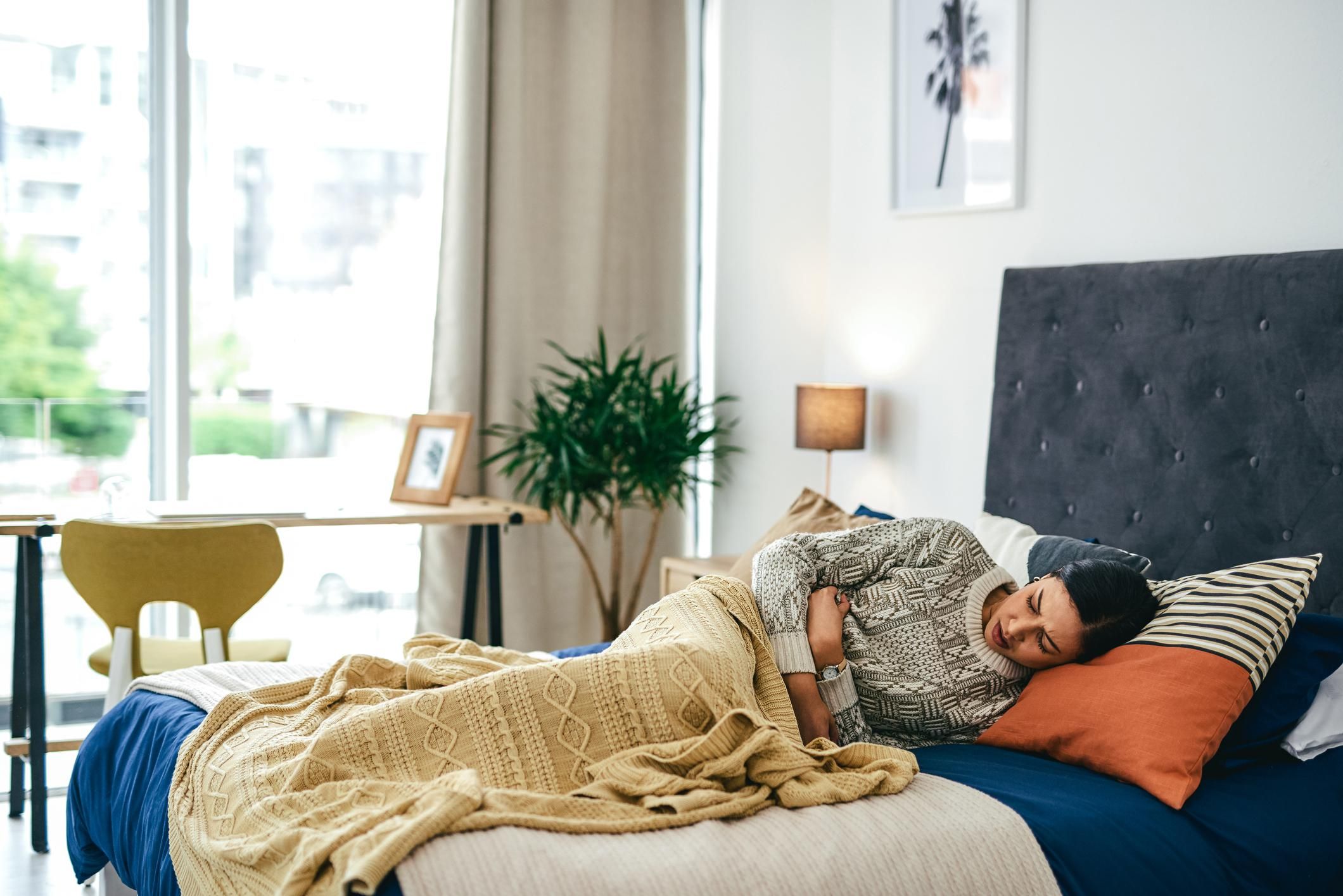 young woman experiencing stomach pain while lying on her bed at home
