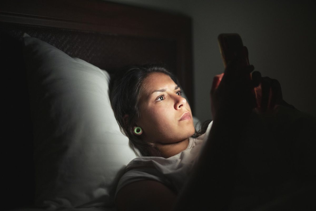 Young woman laying in bed and using smart phone at low light.