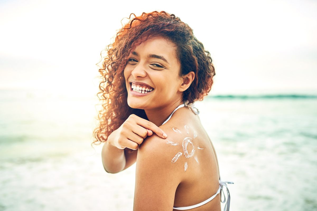 young woman pointing at sunscreen on her back at the beach