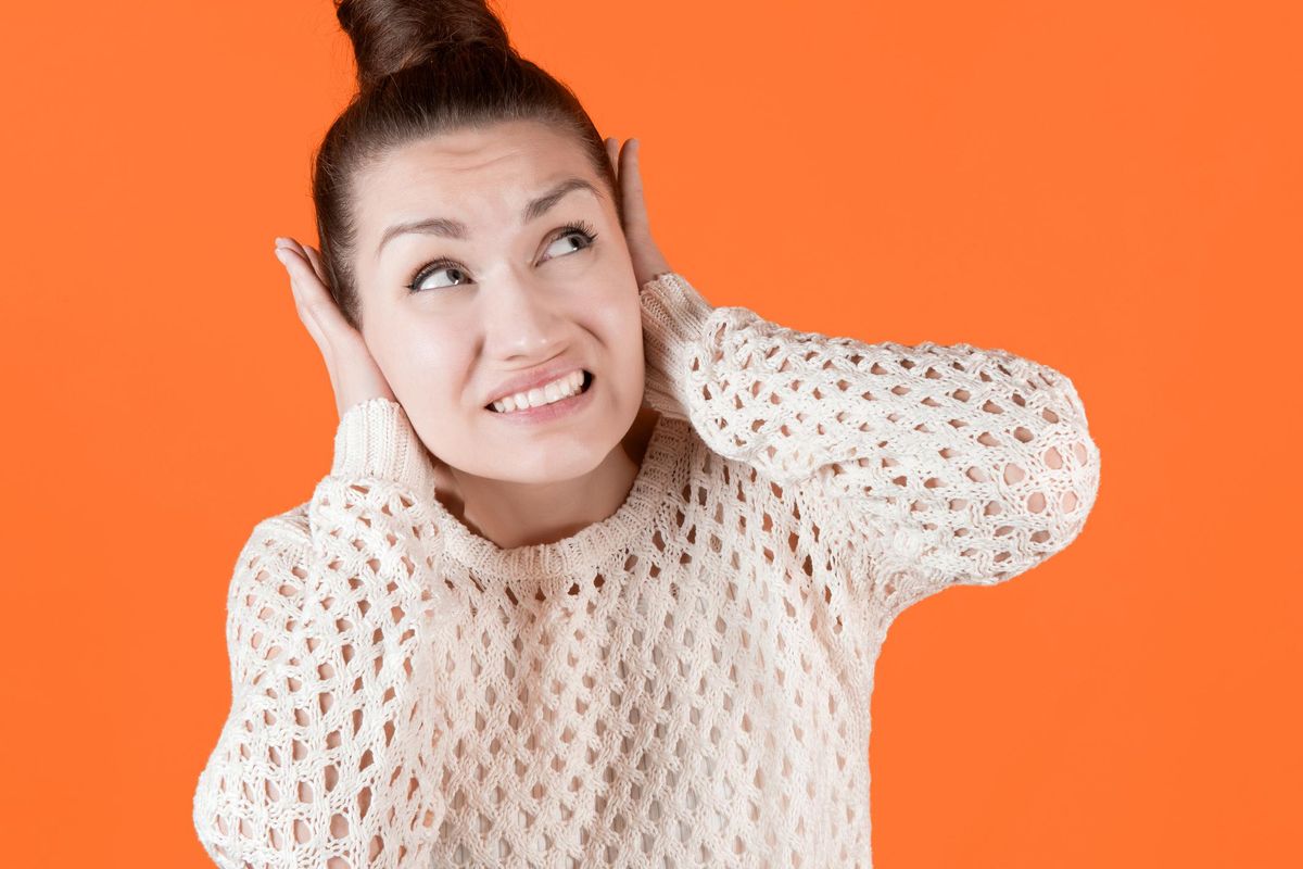 Young woman tightly covers her ears with her hands